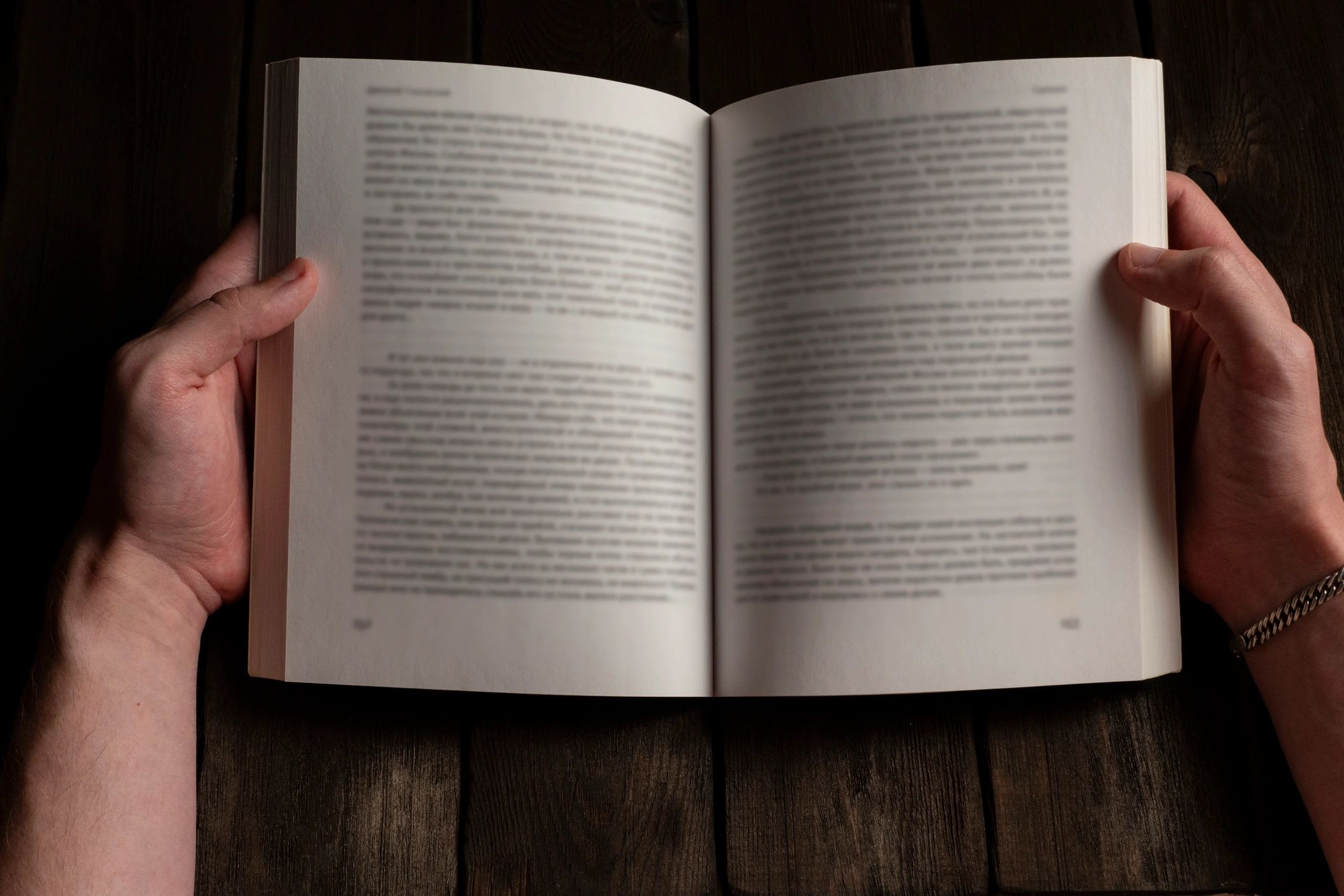 Hands holding an open book on a wooden table