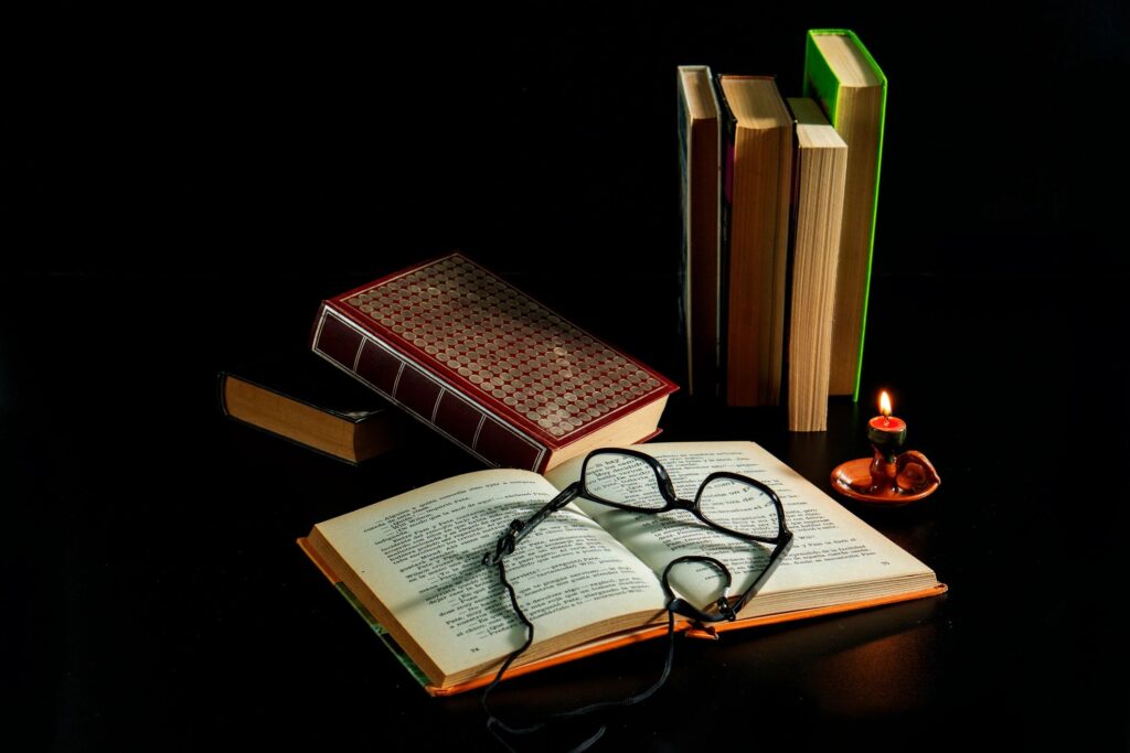 A book is open on a table with a candle and a pair of glasses